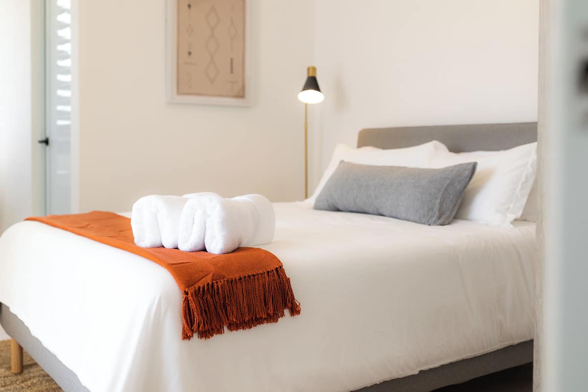 A neatly made bed with white linens, a grey pillow, and a brown throw blanket.