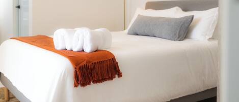 A neatly made bed with white linens, a grey pillow, and a brown throw blanket.