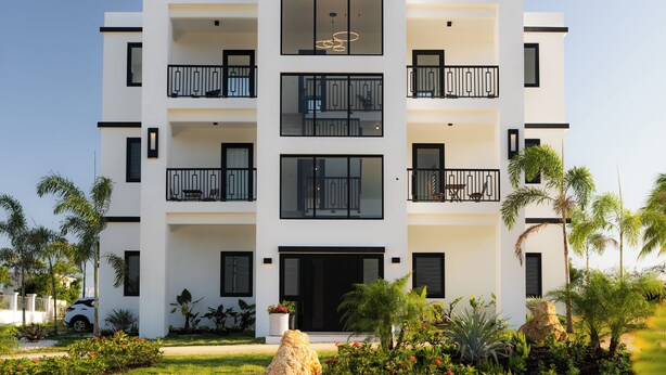 A modern multi-story building with balconies, large windows, and a well-maintained garden with tropical plants. - Outsite Puerto Rico Aguadilla - Work, Connect, Explore (Aguacate)