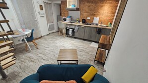 Un salon moderne avec un canapé bleu, une table basse en bois et un coin cuisine équipé d’un four à micro-ondes, d’une bouilloire et de meubles de rangement en bois.