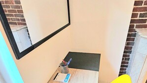Une petite pièce d’angle avec une table en bois, une chaise jaune, un miroir et un mur en briques.