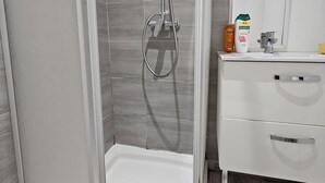 Une douche avec une porte en verre, un meuble-lavabo blanc doté de deux tiroirs et un miroir au-dessus du meuble-lavabo.