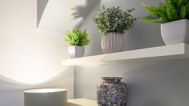 Ein modernes Interieur mit einer Stehlampe, drei Regalen mit Dekoration und einem geometrischen Wandmuster.