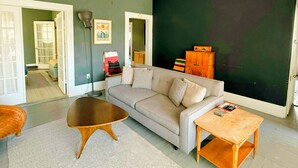 Ein Wohnzimmer mit Deckenventilator, einem grauen Sofa, einem runden Couchtisch und einem Holznachttisch.