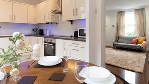 A modern kitchen with white cabinets, a built-in oven, and a microwave. There is a dining table set with plates, glasses, and a vase with flowers.
