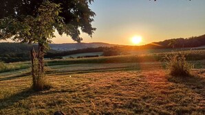 A sunset over a grassy field with trees and distant hills. - Cozy, newly renovated vacation apartment "Merlin" in the heart of the Taunus! (Weilrod)