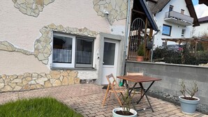 A house with a stone facade, a wooden table and chairs outside, and two potted plants. - Cozy, newly renovated vacation apartment "Merlin" in the heart of the Taunus! (Weilrod)