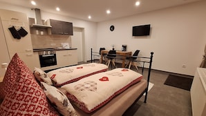 A compact bedroom with a bed, bedside tables, a small desk, and a kitchenette. - Cozy, newly renovated vacation apartment "Merlin" in the heart of the Taunus! (Weilrod)
