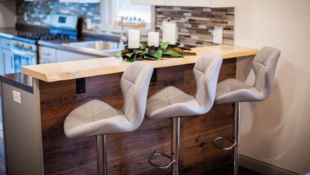 A kitchen with a wooden island, two bar stools, and a backsplash.