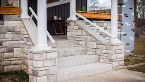 A stone staircase leading to a porch with white railings and a wooden bench.