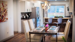 A modern kitchen with white cabinets, a stainless steel refrigerator, and a dining area with a glass table and chairs.