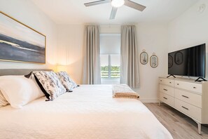 A bedroom with a bed, a ceiling fan, a TV, and a window with curtains. - Sarasota: Charming 2 bdrm Condo w/Resort Pool (Sarasota)