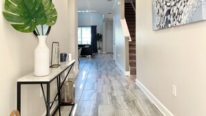 A hallway with a marble floor, a white console table with a large green plant, a black metal console, and a modern light fixture. - Luxury 5-bedroom near Disney, Clubhouse Resort, Private Pool & Spa (Kissimmee)