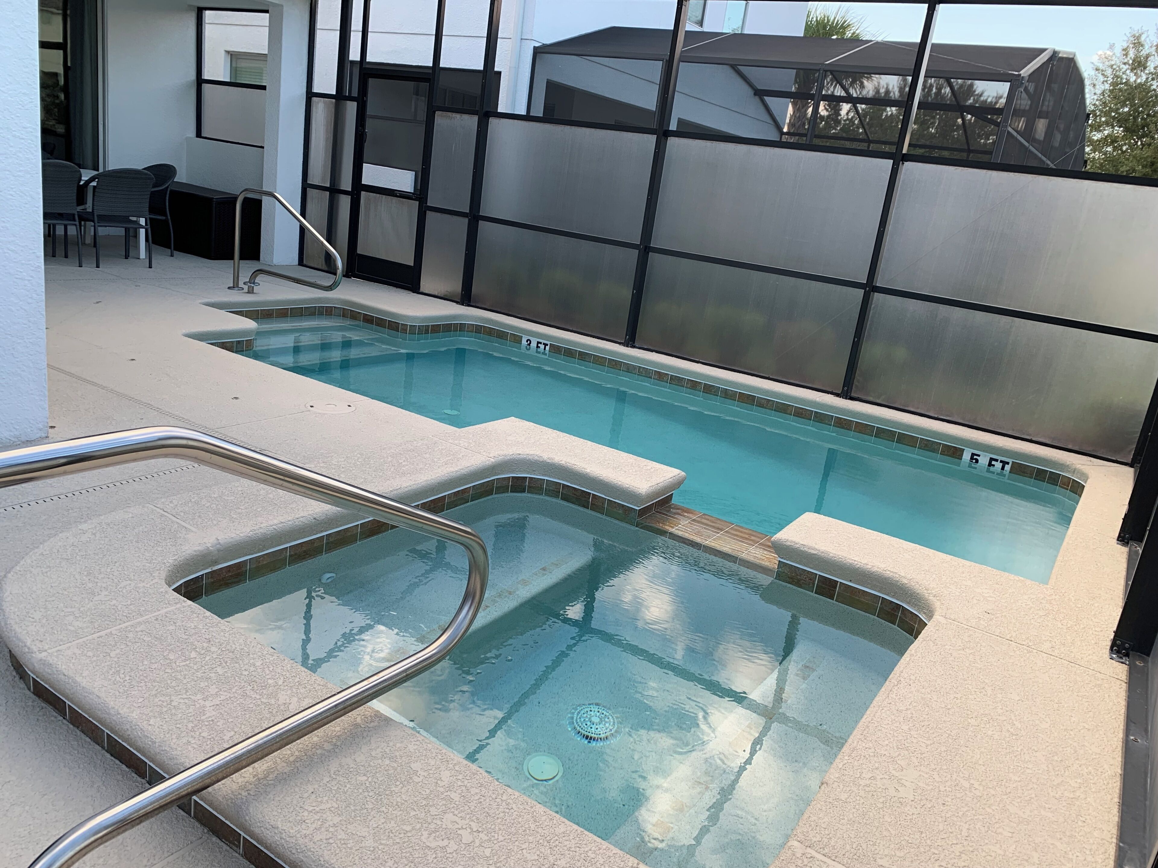 A swimming pool with a glass barrier, a metal handrail, and a tiled deck.
