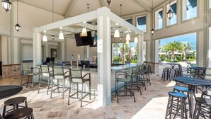 A spacious outdoor bar area with multiple seating options, a central island with a bar counter, and a television mounted above the bar. - Luxury 5-bedroom near Disney, Clubhouse Resort, Private Pool & Spa (Kissimmee)