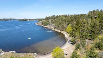 Ett kustlandskap med fri utsikt över strandlinjen, en liten brygga och ett tätbevuxet skogsområde.