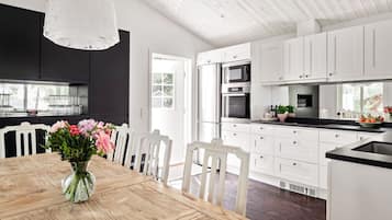 Ett modernt kök med vita köksskåp, ett matbord i trä och en vas med blommor.