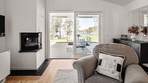 A modern living room with a fireplace, sliding glass doors to a patio, and a dining area. - Seaside Serenity, Modern Family Retreat (Värmdö)