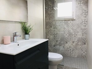 A bathroom with a white sink, a pink cup, a potted plant, a toilet, and patterned tiles. - Renovated apartment in Roses, near beach and center, sleeps 6. (Roses)