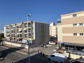A multi-story building with balconies, a street with cars, and a restaurant with outdoor seating. - Cozy T1 with underground garage (Balaruc-les-Bains)