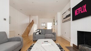 A modern living room with a grey sofa, a black and white striped sofa, a white coffee table with a book, a staircase leading to another room, and a black and white abstract painting on the wall. - Fulham Spacious 4BD Home | Parking & Garden | WiFi (London)