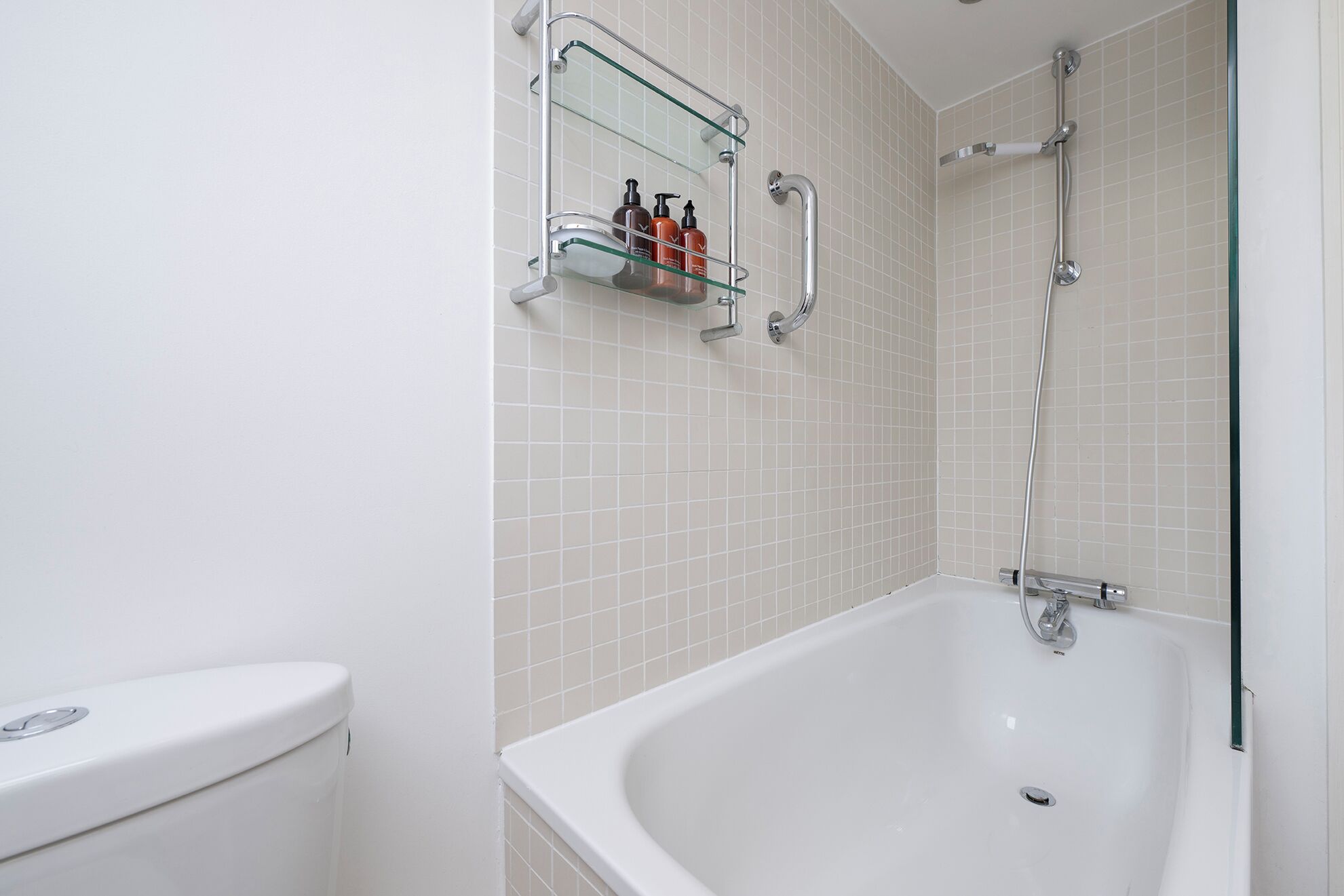 A bathroom with a white bathtub, a glass shelf with toiletries, and a shower area.