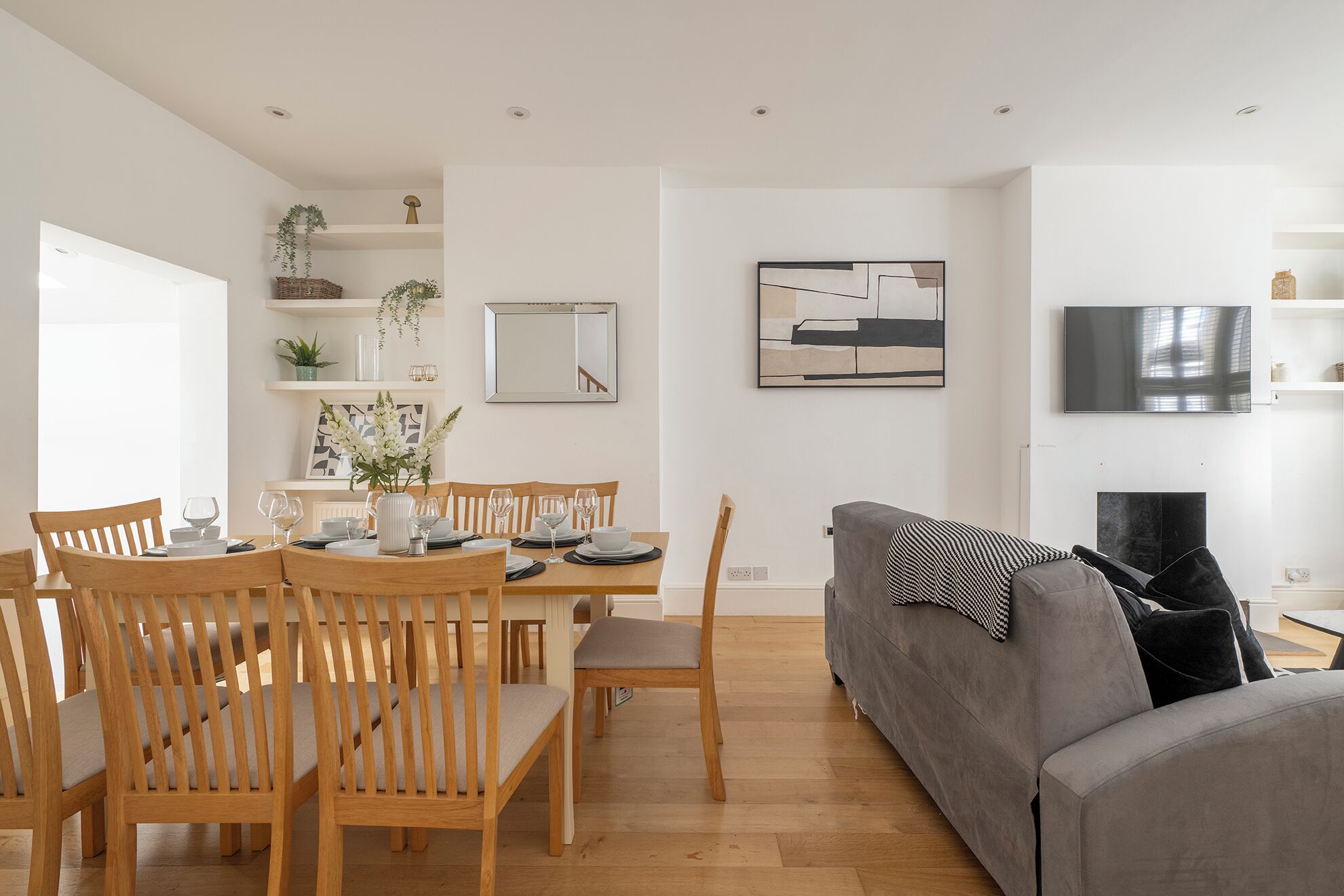 Un salon moderne comprenant un coin repas, des meubles en bois, un canapé gris et un téléviseur à écran plat fixé au mur.