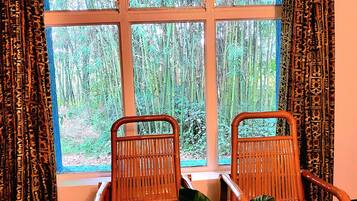 Une pièce avec deux fauteuils en osier placés face à une fenêtre donnant sur une forêt de bambous.