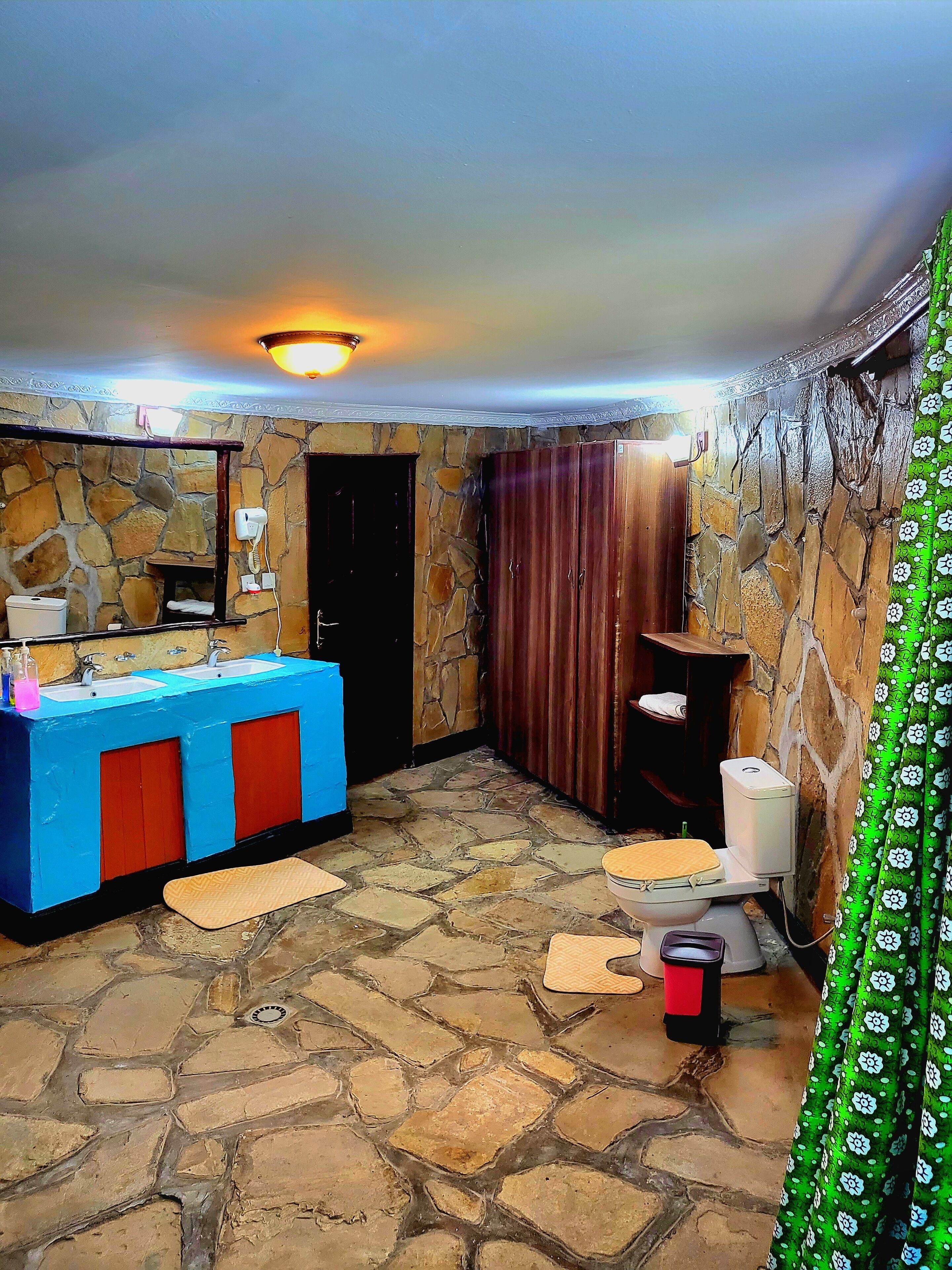 A bathroom with a stone wall, a blue sink, a wooden cabinet, and a toilet.