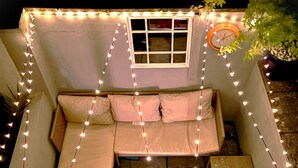 Un espace extérieur accueillant avec un banc rembourré, une petite table et des guirlandes lumineuses.