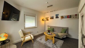 Un salon chaleureux avec un canapé, une chaise en bois, une petite table ronde, un globe terrestre sur un pied, un téléviseur fixé au mur et une fenêtre avec des stores.