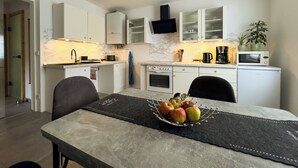 Une cuisine moderne avec des meubles blancs, un pare-feu en marbre et un coin repas avec une table dressée pour quatre personnes.