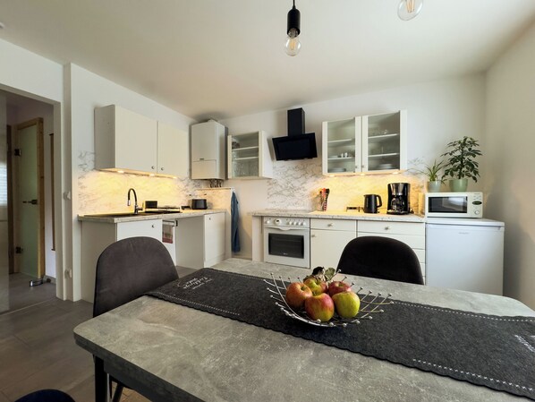A modern kitchen with white cabinets, a marble backsplash, and a dining area with a table set for four.