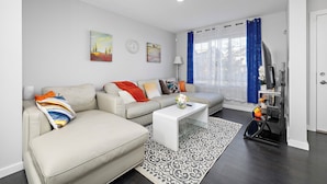A modern living room with a beige sofa, a white coffee table, and a patterned rug. - Laurel Modern Haven (Edmonton)
