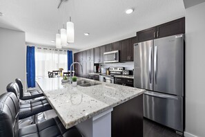A modern kitchen with stainless steel appliances, a marble countertop, and a dining area with leather chairs. - Laurel Modern Haven (Edmonton)