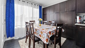 A dining area with a table set for four, surrounded by dark wooden cabinets and a kitchen area with modern appliances. - Laurel Modern Haven (Edmonton)