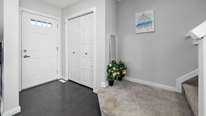 A hallway with a carpeted floor, white walls, and a door with frosted glass panels. - Laurel Modern Haven (Edmonton)
