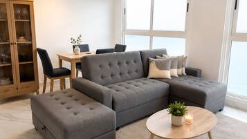 A modern living room with a sectional sofa, a round coffee table, a dining area with chairs, and a cabinet with glass doors.