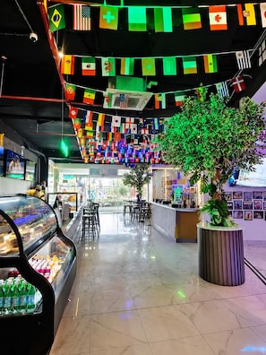 A modern interior with a central seating area, a glass display case with bottled beverages, and a variety of flags hanging from the ceiling. - Apartments at The Sands – Ocean View Panama City (Panama City)