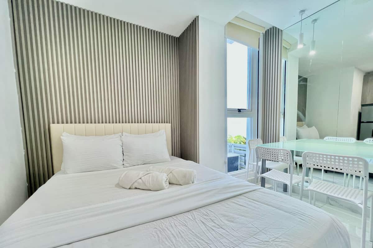 Una habitación de hotel moderna con una cama grande, una mesa de vidrio, sillas y un balcón con vistas.