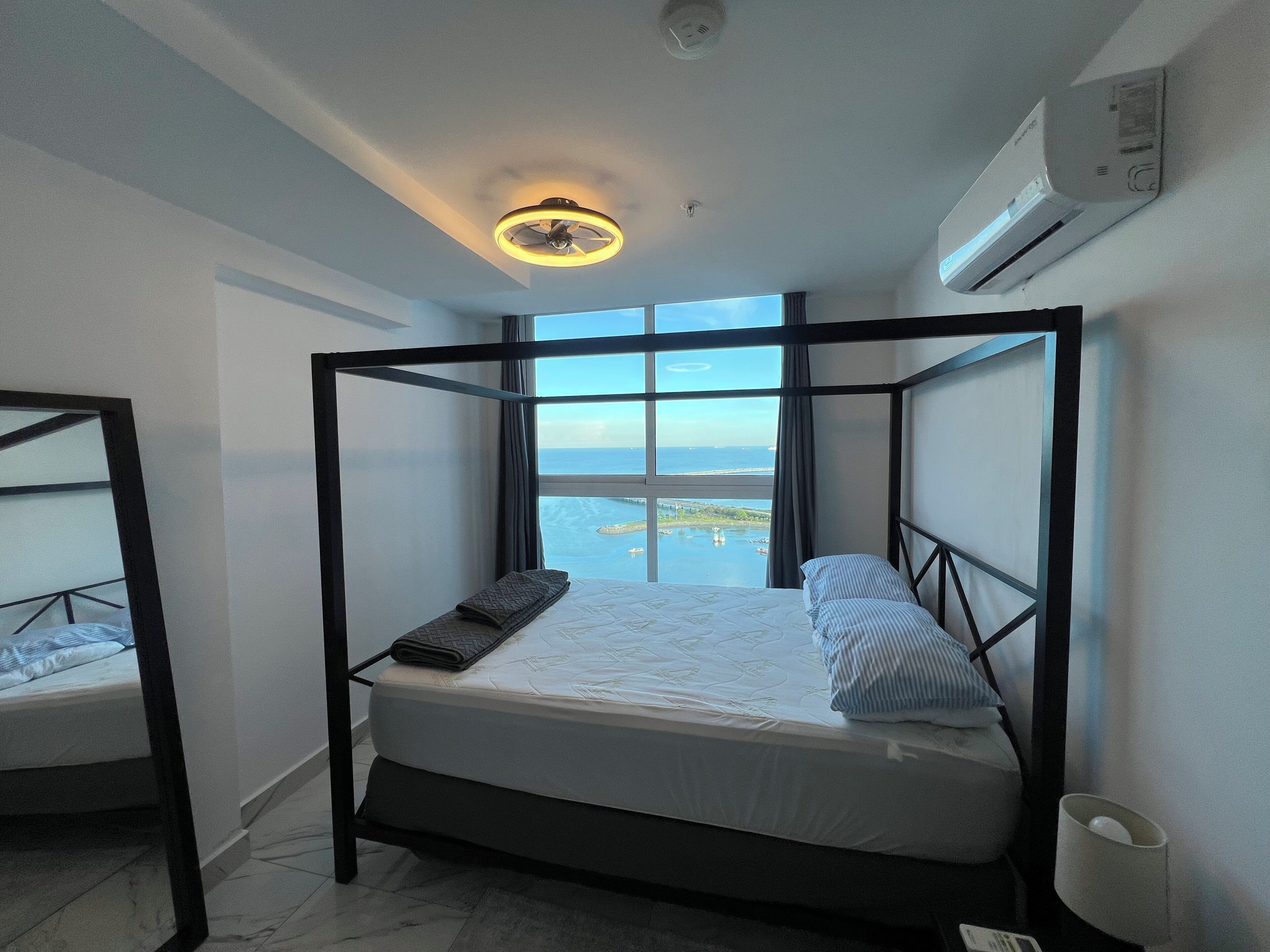 Una cama con dosel y vistas al mar, un ventilador de techo y un equipo de aire acondicionado.