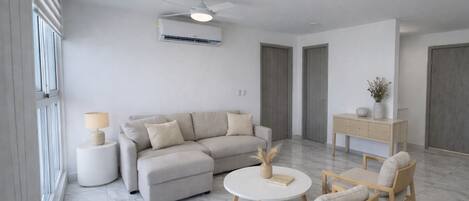 A modern living room with a sofa, two armchairs, a coffee table, a lamp, a side table, a ceiling fan, an air conditioning unit, and a cabinet.