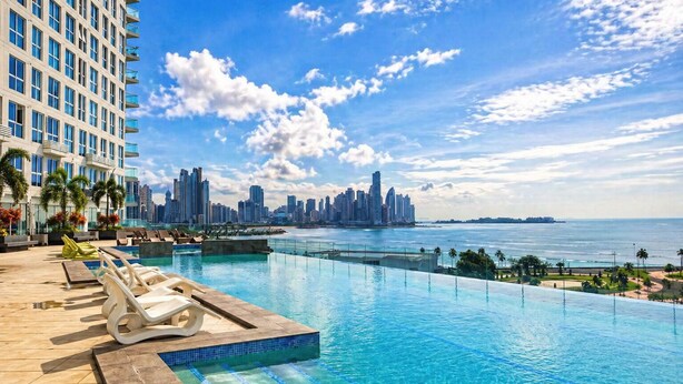 A rooftop infinity pool with a city skyline view, lounge chairs, and palm trees. - Apartments at The Sands – Ocean View Panama City (Panama City)