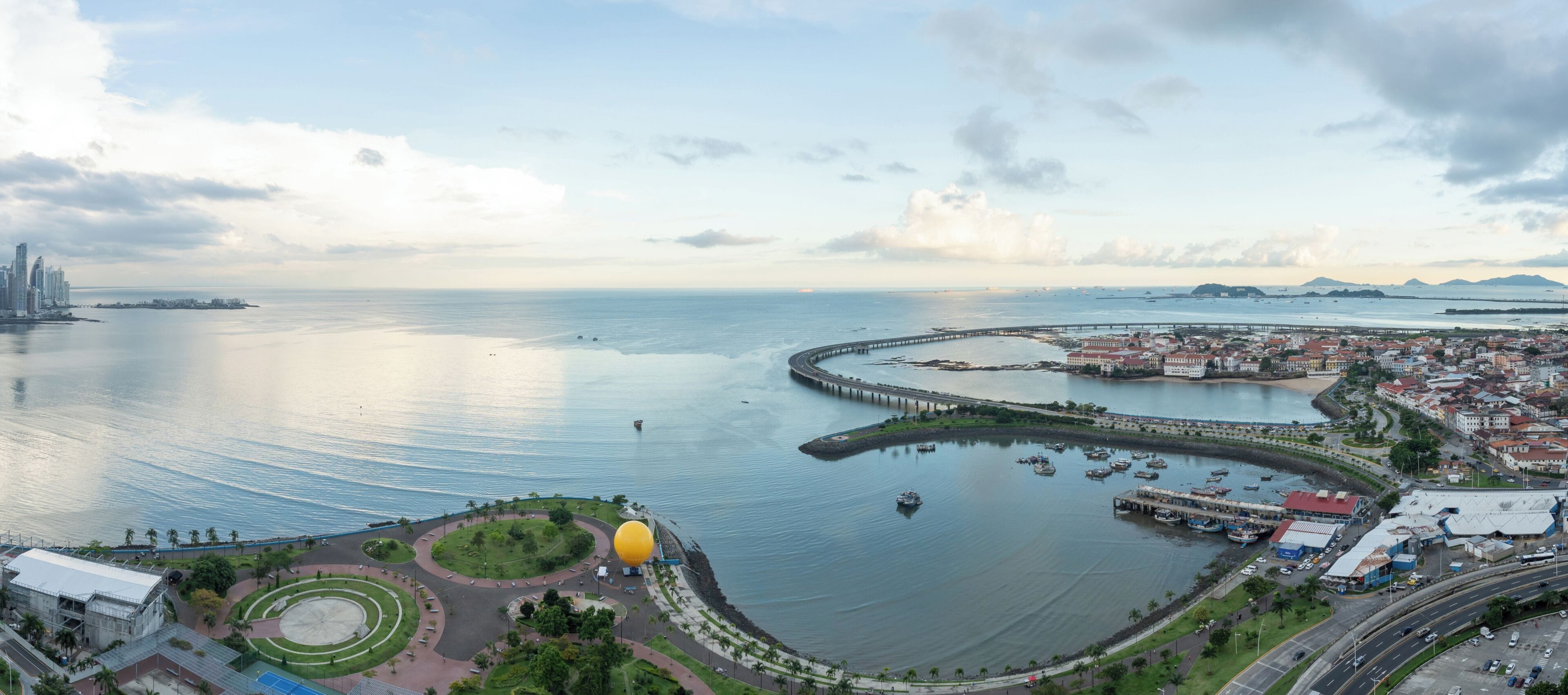 Un paysage urbain côtier avec un port de plaisance, un rond-point et une grande structure en forme de dôme jaune.