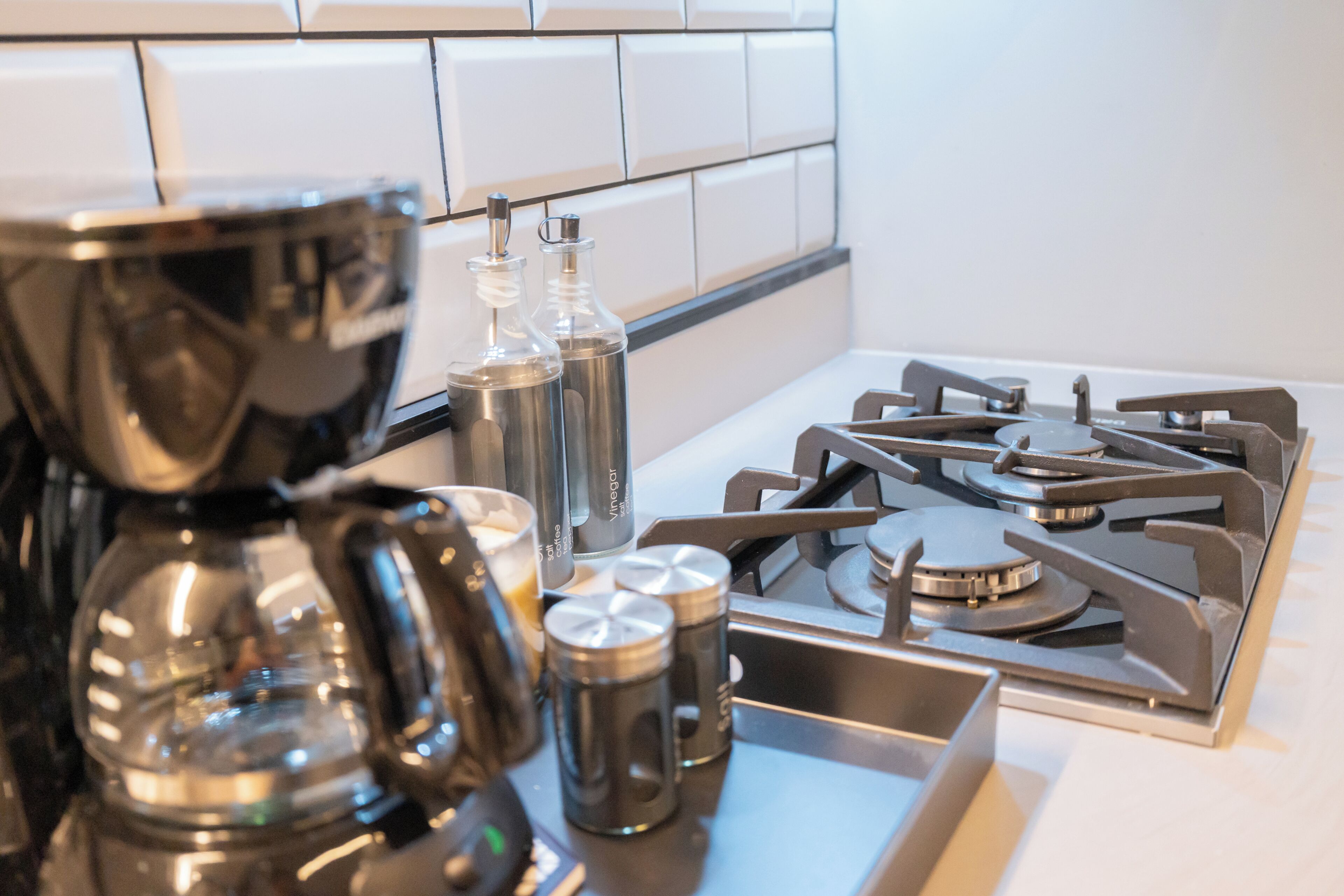 Una cocina con estufa a gas, cafetera y botellas de condimentos.