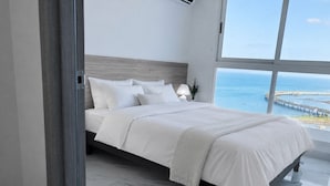 A modern bedroom with a large bed, a nightstand, and a view of the ocean. - Apartments at The Sands – Ocean View Panama City (Panama City)