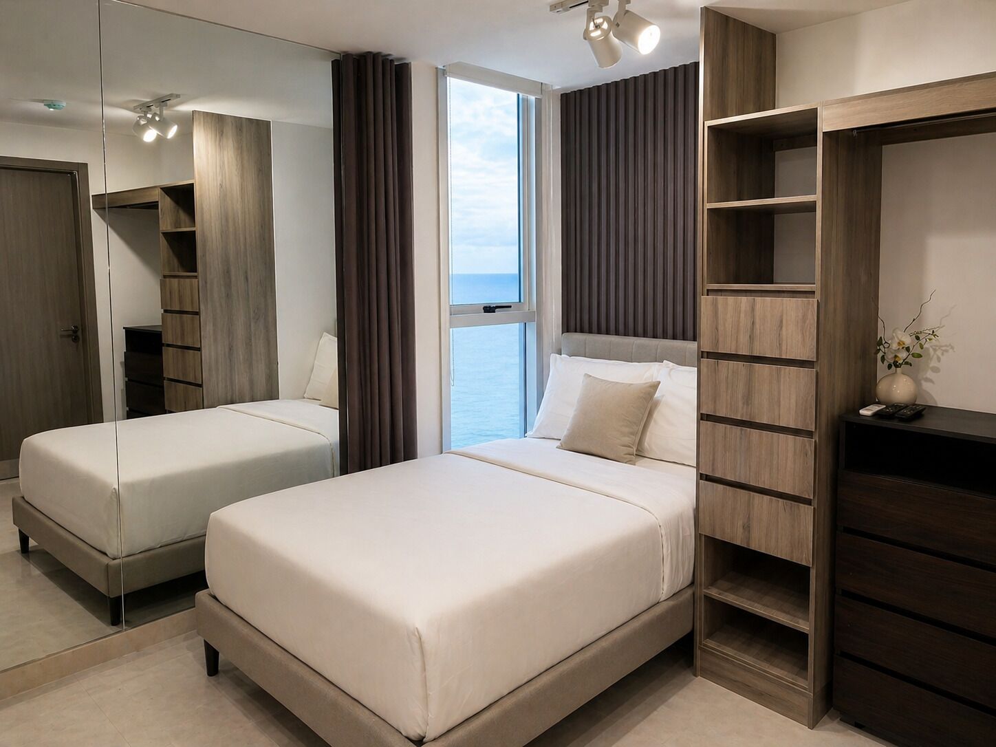 A hotel room with two beds, a large mirror, a wardrobe, and a view of the sea.