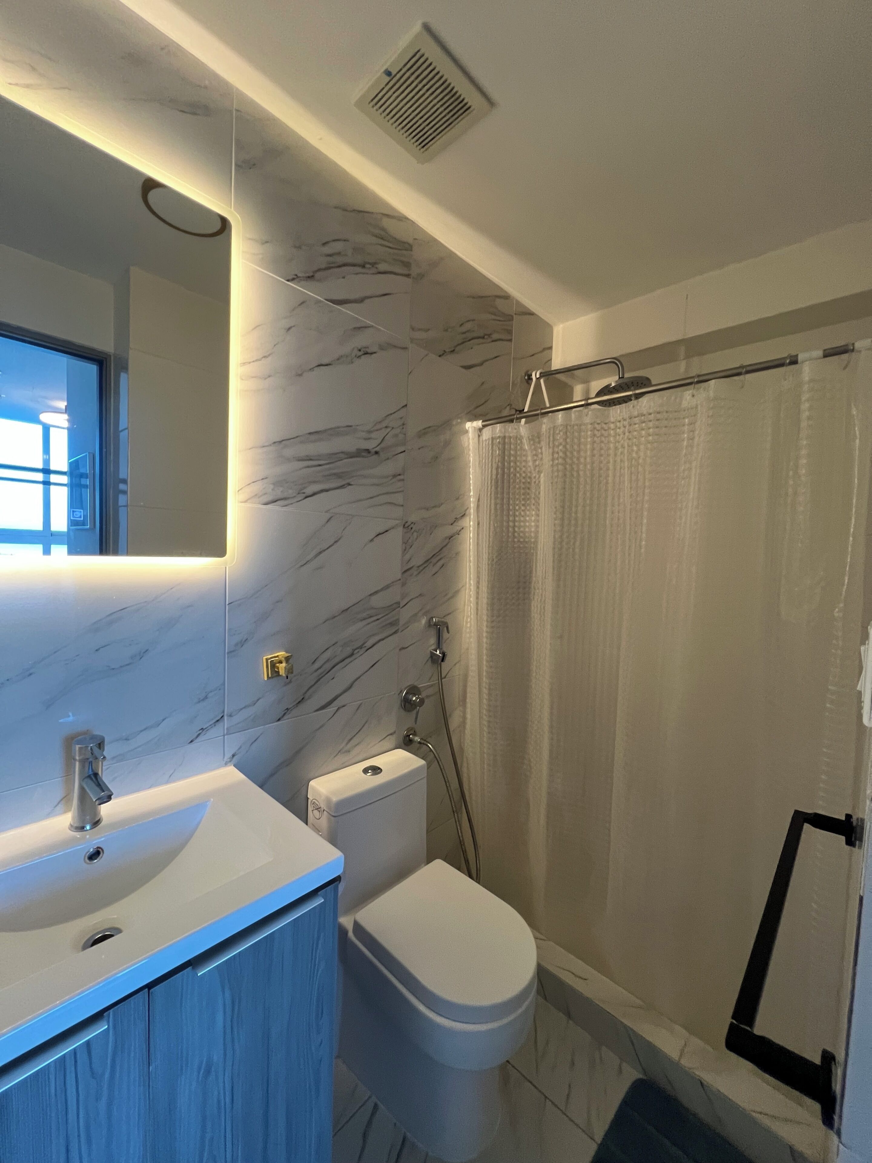 A bathroom with a marble wall, a sink, a toilet, and a shower curtain.