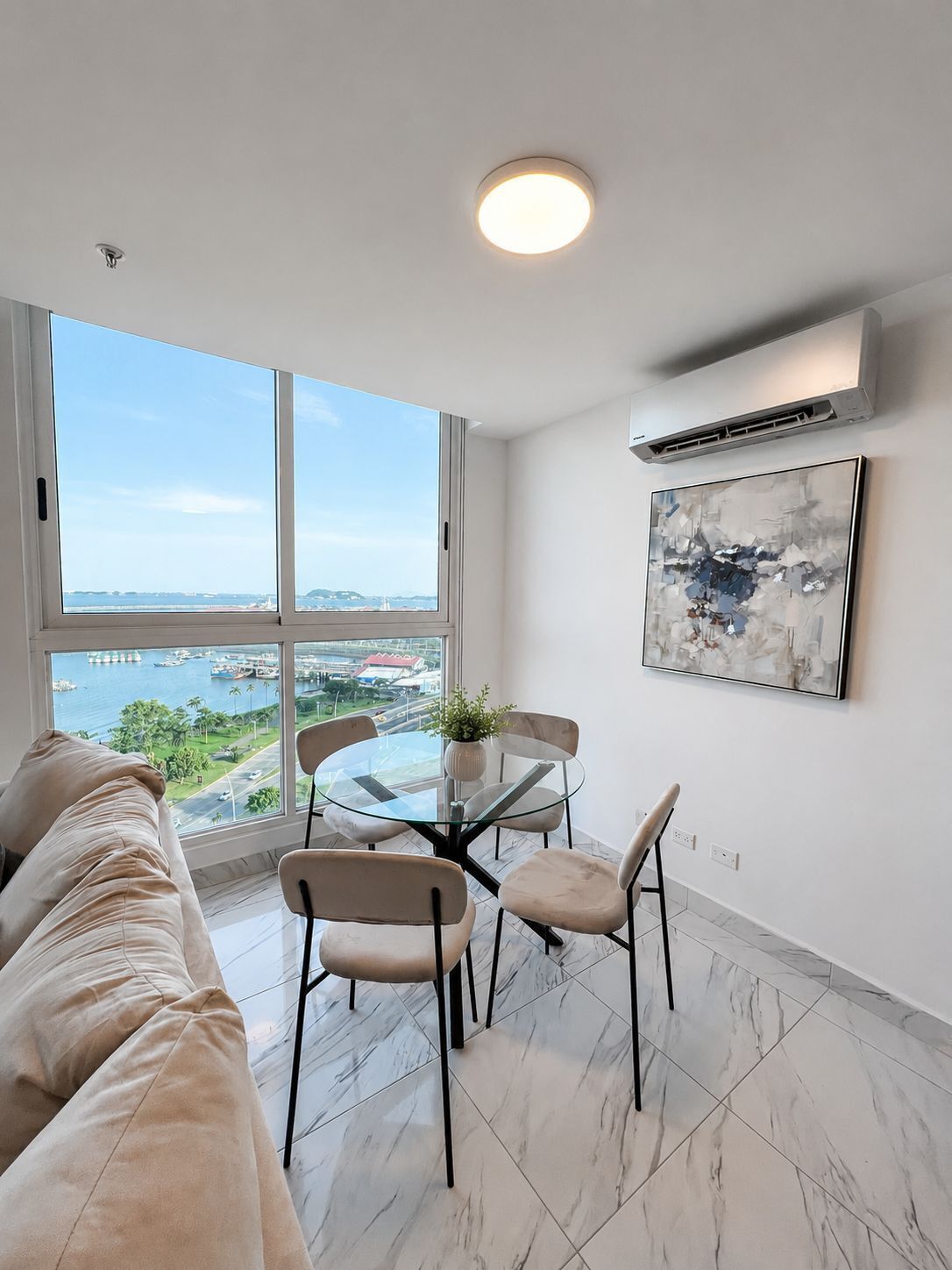 Ein modernes Wohnzimmer mit einem Glastisch, einem beigen Sofa und einem großen Fenster mit Blick auf die Stadt.