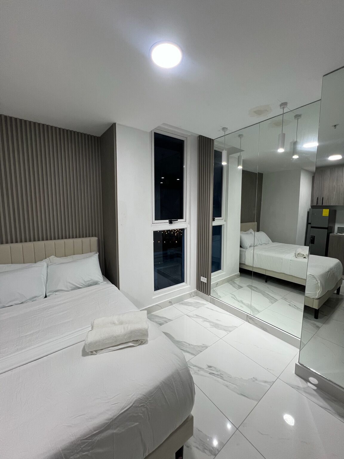 Una habitació d'hotel moderna amb un llit gran, una tauleta de nit, un mirall i vistes de la ciutat de nit.